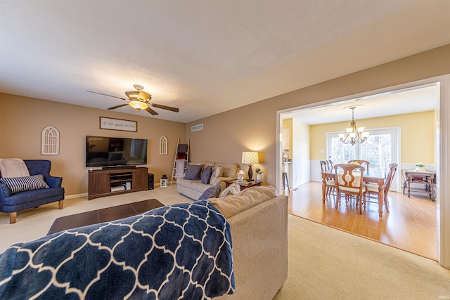 carpeted living room featuring ceiling fan with notable chandelier