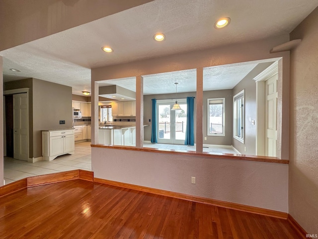 interior space featuring light wood-type flooring, pendant lighting, a textured ceiling, and baseboards