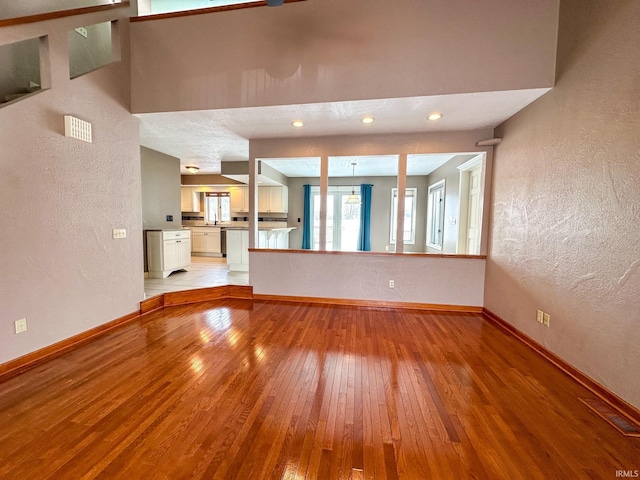 unfurnished living room with light wood-style floors, a textured wall, and baseboards