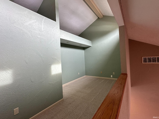 carpeted empty room with visible vents, a textured wall, lofted ceiling with beams, and baseboards