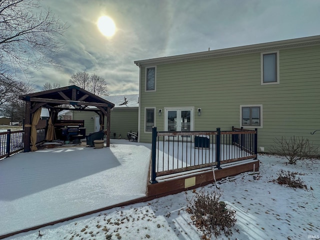 snow covered back of property with a deck, french doors, and a gazebo