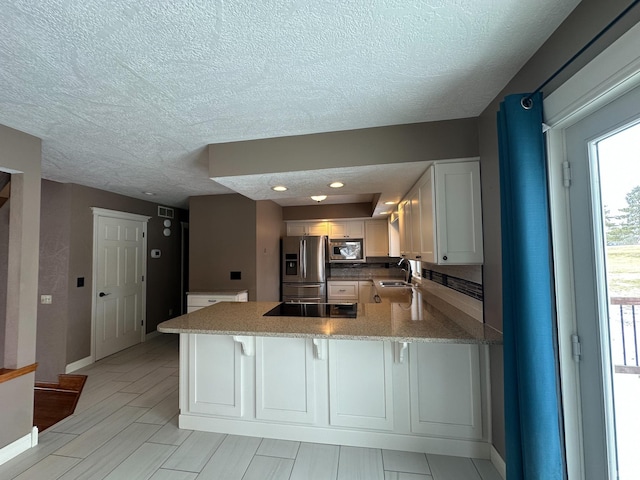 kitchen with appliances with stainless steel finishes, white cabinets, a sink, a peninsula, and a kitchen bar