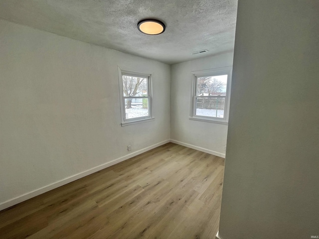 spare room featuring baseboards, a textured ceiling, visible vents, and light wood-style floors