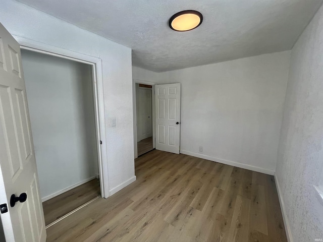 unfurnished bedroom with baseboards, a closet, a textured ceiling, and light wood-style floors