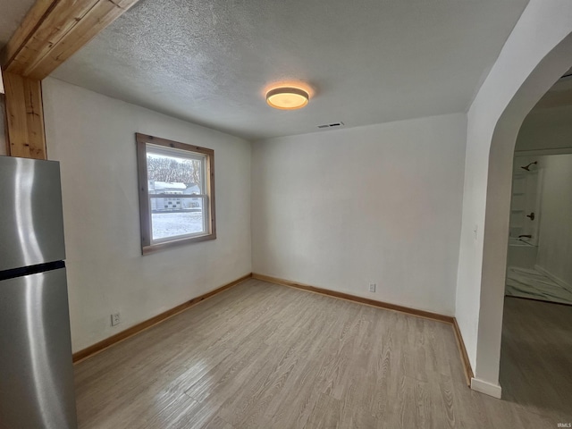 interior space featuring arched walkways, visible vents, a textured ceiling, light wood-type flooring, and baseboards