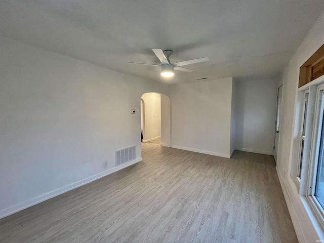 unfurnished room with arched walkways, visible vents, light wood-style flooring, ceiling fan, and baseboards