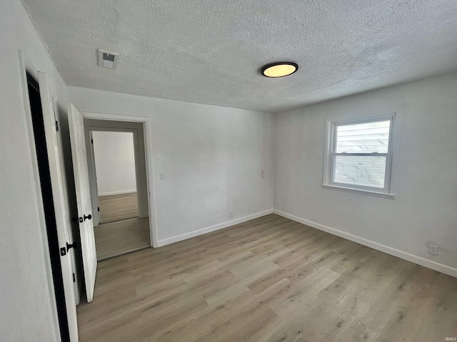 unfurnished room with baseboards, a textured ceiling, visible vents, and light wood-style floors