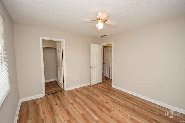 unfurnished bedroom featuring ceiling fan, a closet, a textured ceiling, and light wood-type flooring