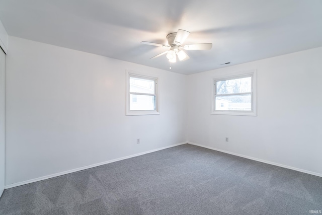 unfurnished room with dark colored carpet, a healthy amount of sunlight, and ceiling fan