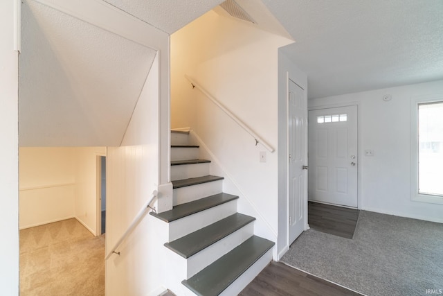 stairway with a textured ceiling and carpet flooring