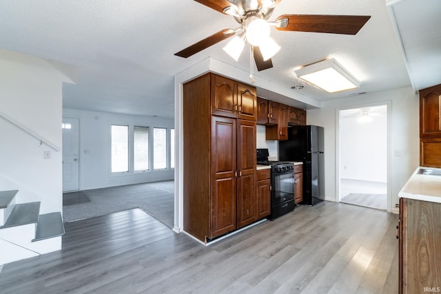 kitchen featuring light wood-type flooring, a textured ceiling, ceiling fan, and black appliances