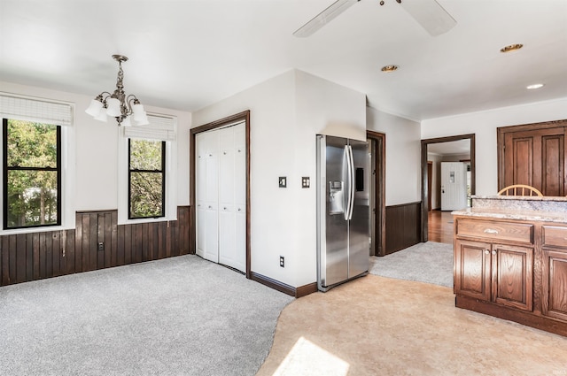 interior space featuring pendant lighting, an inviting chandelier, light carpet, stainless steel fridge with ice dispenser, and wood walls