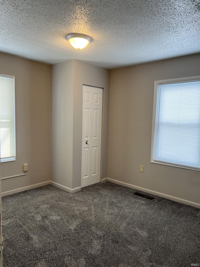 empty room featuring a textured ceiling, a healthy amount of sunlight, and dark colored carpet