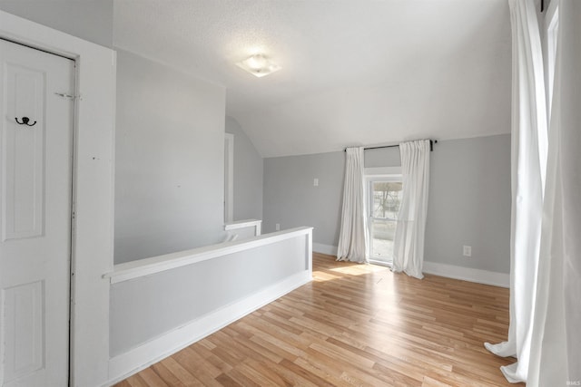 hall featuring vaulted ceiling, a textured ceiling, and light hardwood / wood-style floors