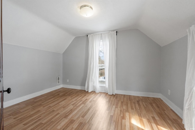 bonus room featuring lofted ceiling, a textured ceiling, and light hardwood / wood-style floors