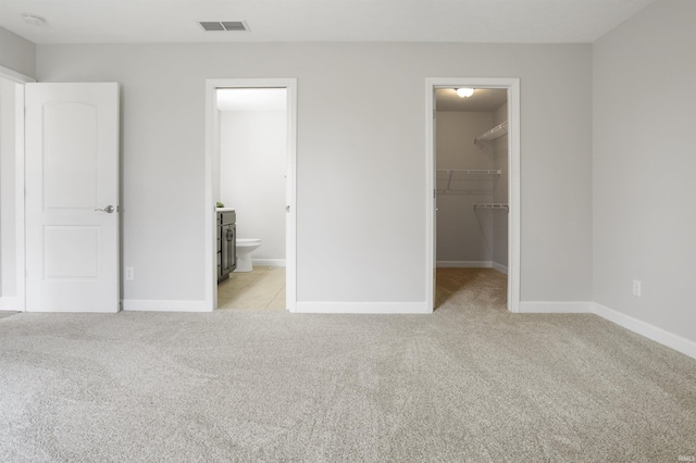 unfurnished bedroom featuring light carpet, connected bathroom, a spacious closet, and a closet