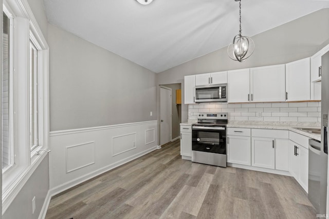 kitchen featuring hanging light fixtures, vaulted ceiling, stainless steel appliances, and white cabinets