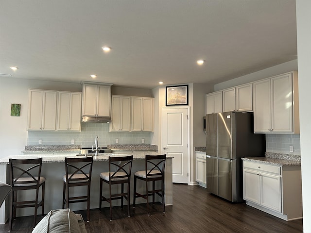 kitchen with white cabinets, a kitchen bar, stainless steel fridge, and light stone counters