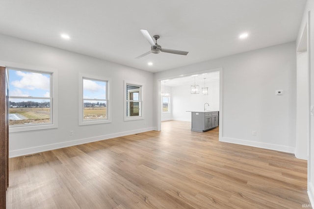 unfurnished living room featuring sink, ceiling fan with notable chandelier, and light wood-type flooring