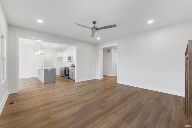 unfurnished living room with sink, ceiling fan with notable chandelier, and dark hardwood / wood-style flooring