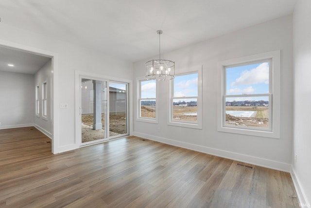 unfurnished dining area featuring an inviting chandelier and wood-type flooring