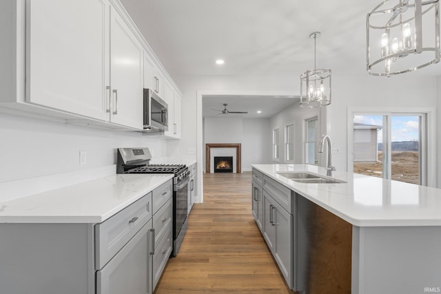 kitchen with sink, a kitchen island with sink, white cabinetry, stainless steel appliances, and light wood-type flooring