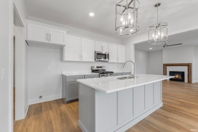 kitchen featuring appliances with stainless steel finishes, decorative light fixtures, an island with sink, sink, and white cabinets