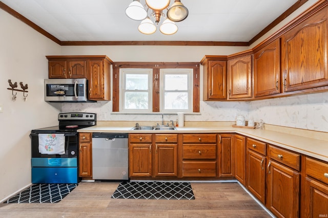 kitchen featuring sink, light hardwood / wood-style flooring, ornamental molding, appliances with stainless steel finishes, and a notable chandelier