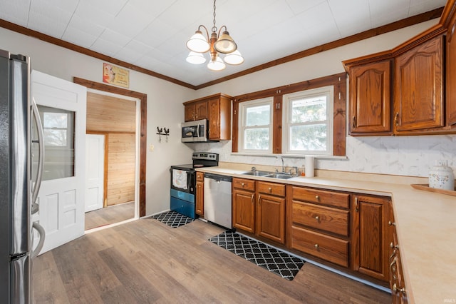 kitchen with sink, hardwood / wood-style flooring, ornamental molding, appliances with stainless steel finishes, and pendant lighting