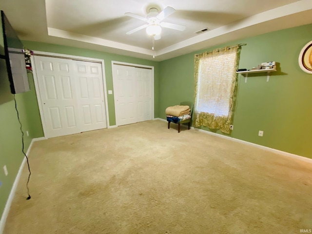 unfurnished bedroom featuring a raised ceiling, light carpet, multiple closets, and ceiling fan