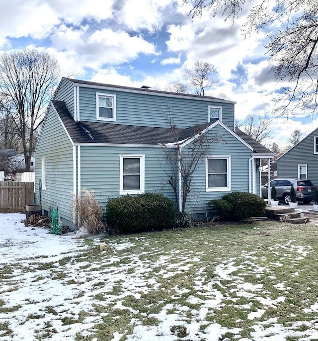 snow covered back of property with a shingled roof and fence