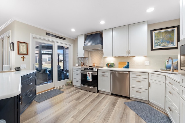 kitchen featuring wall chimney range hood, sink, stainless steel appliances, white cabinets, and light wood-type flooring