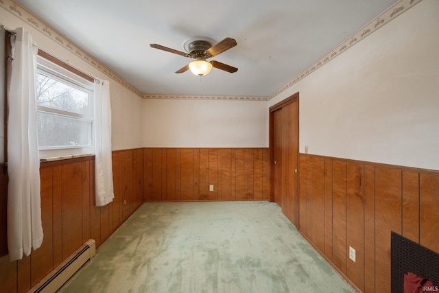 carpeted spare room with a baseboard radiator, ceiling fan, and wooden walls