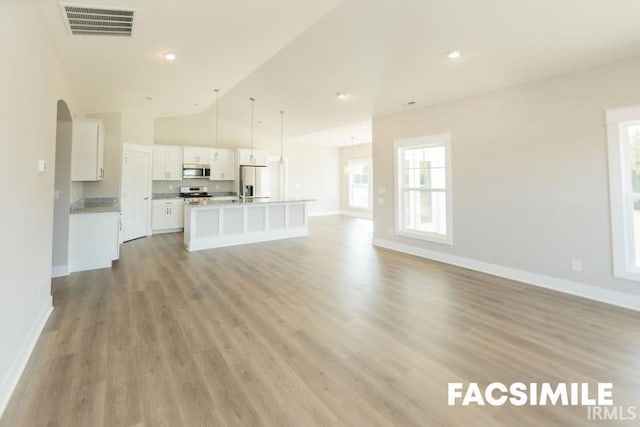 unfurnished living room featuring a healthy amount of sunlight, high vaulted ceiling, and light wood-type flooring