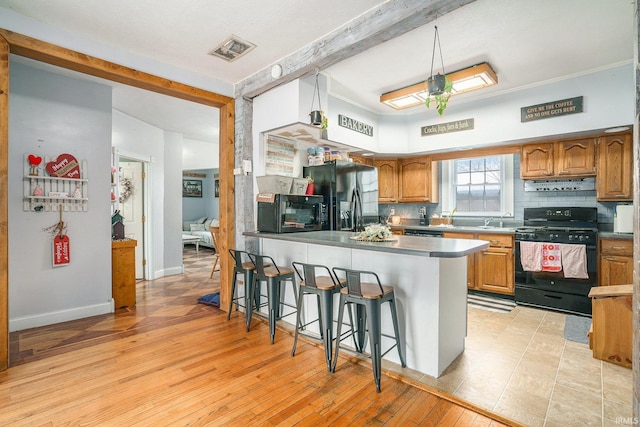 kitchen featuring a breakfast bar area, tasteful backsplash, extractor fan, black appliances, and light wood-type flooring