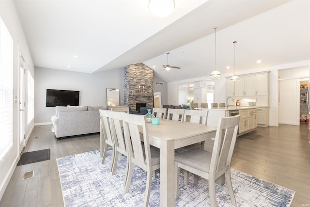 dining space featuring sink, ceiling fan, hardwood / wood-style floors, a stone fireplace, and vaulted ceiling