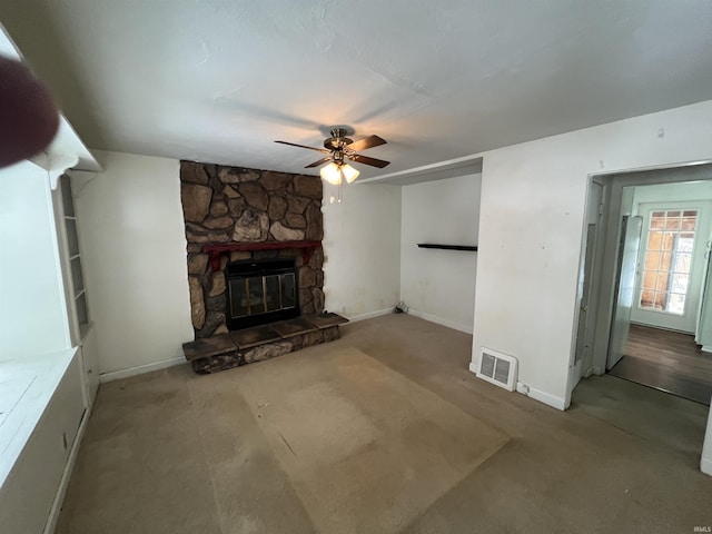 unfurnished living room with ceiling fan, a stone fireplace, and carpet floors