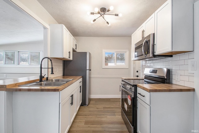 kitchen featuring sink, light hardwood / wood-style flooring, appliances with stainless steel finishes, white cabinetry, and wood counters