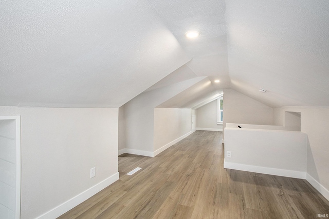 bonus room featuring lofted ceiling, a textured ceiling, and light wood-type flooring