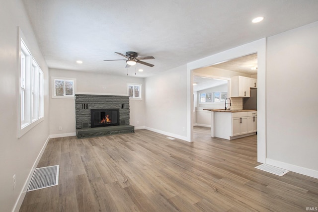 unfurnished living room with sink, a stone fireplace, light hardwood / wood-style floors, and ceiling fan