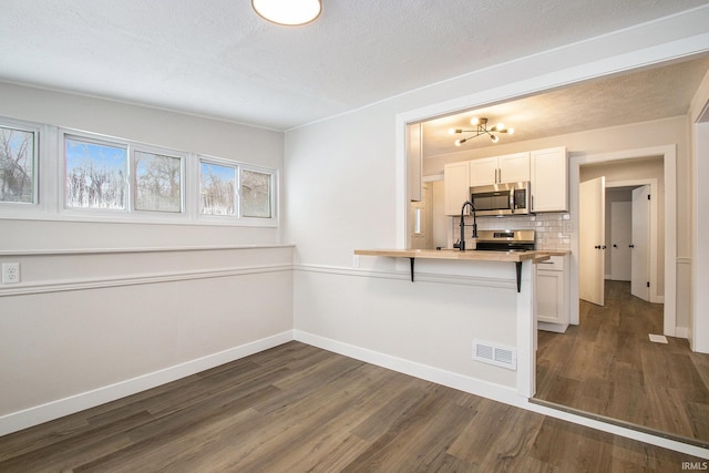 kitchen featuring stainless steel appliances, white cabinetry, dark wood-type flooring, and a kitchen bar