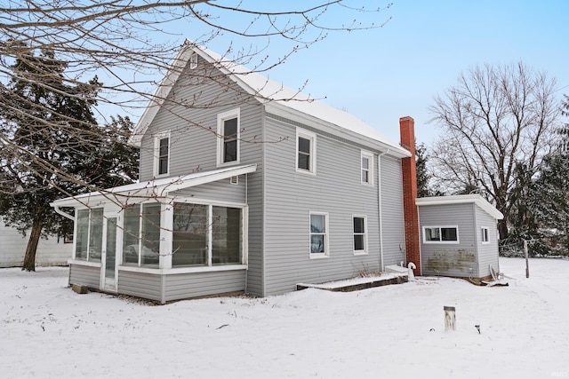 snow covered back of property with a sunroom