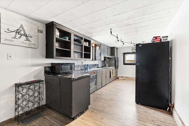 kitchen featuring track lighting, dark stone countertops, light wood-type flooring, and black appliances