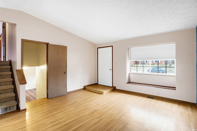 empty room featuring lofted ceiling, light hardwood / wood-style flooring, and a textured ceiling