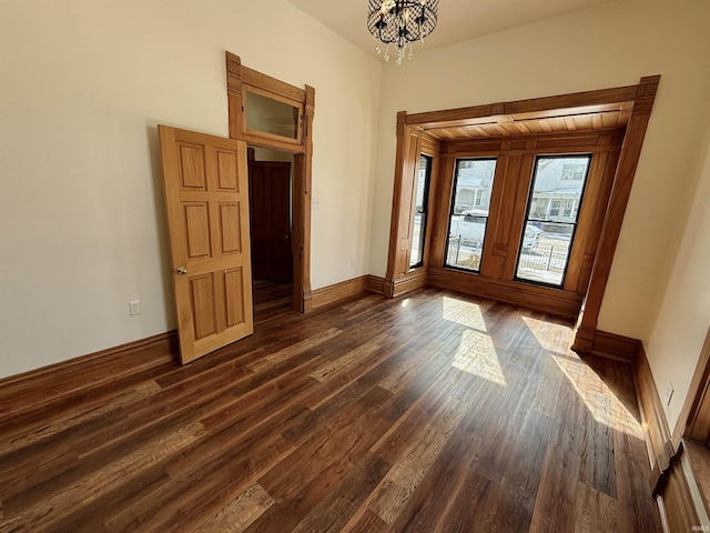 spare room with dark wood-type flooring, a chandelier, and baseboards