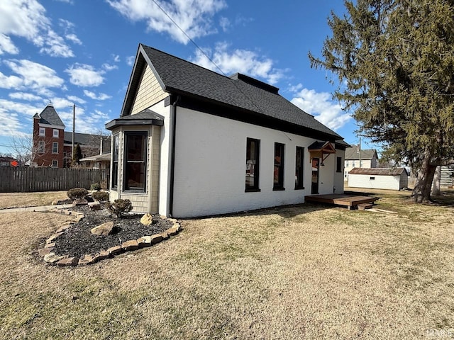 view of side of property featuring a shingled roof, an outbuilding, fence, a yard, and brick siding