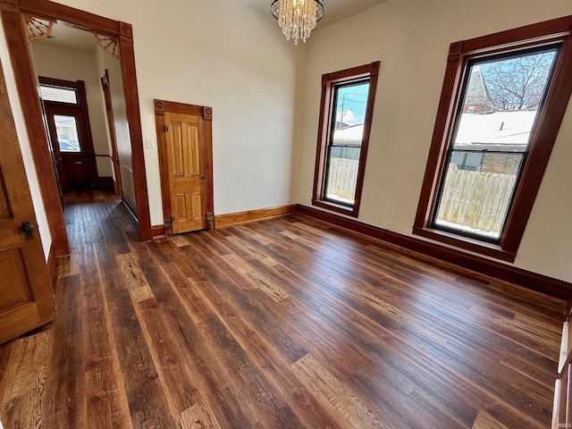 unfurnished room featuring baseboards, dark wood finished floors, a towering ceiling, and a notable chandelier