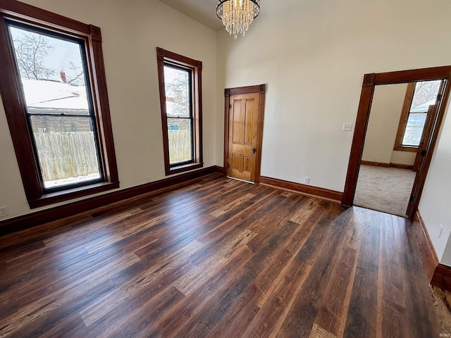 spare room featuring baseboards, dark wood-type flooring, a towering ceiling, and a notable chandelier