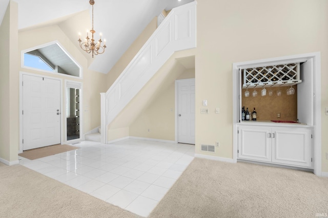 foyer entrance with a chandelier, light colored carpet, and high vaulted ceiling