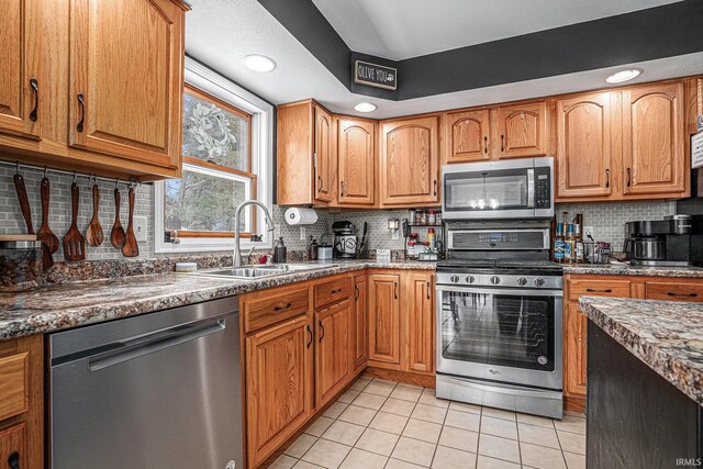 kitchen with dark stone countertops, sink, backsplash, light tile patterned floors, and appliances with stainless steel finishes